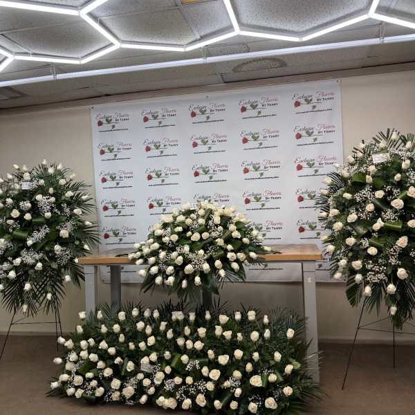 Large white rose funeral sprays and a floor arrangement displayed indoors
