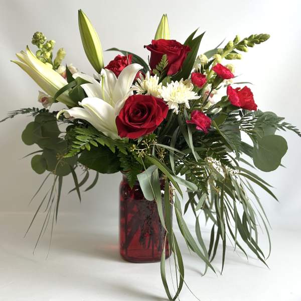 Bouquet of red roses, white lilies, and white mums in a red glass vase
