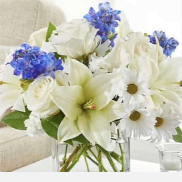 White lilies, daisies, and blue flowers in a clear glass vase