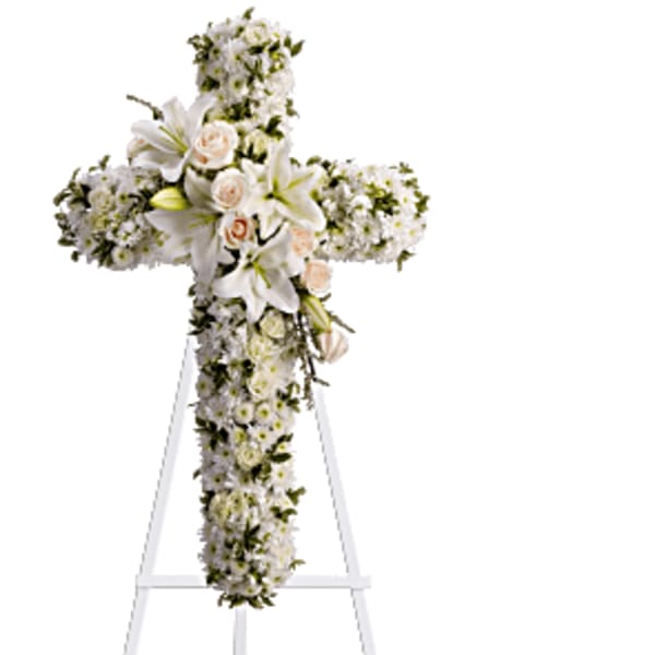 White floral cross arrangement on a stand with lilies and roses