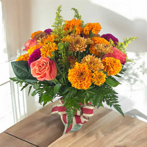 Mixed bouquet of roses, marigolds, and chrysanthemums in a glass vase
