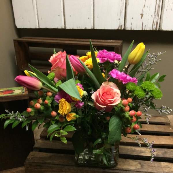 Mixed bouquet of pink roses, tulips, and yellow blooms in a glass vase