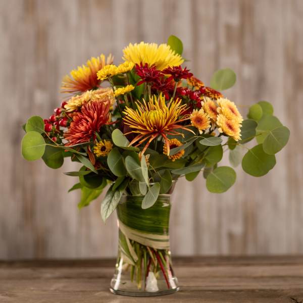 Bouquet of yellow, orange, and red chrysanthemums in a glass vase