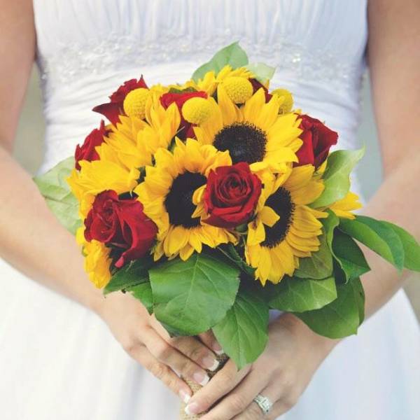 Bride holding a bouquet of sunflowers and red roses with burlap wrap