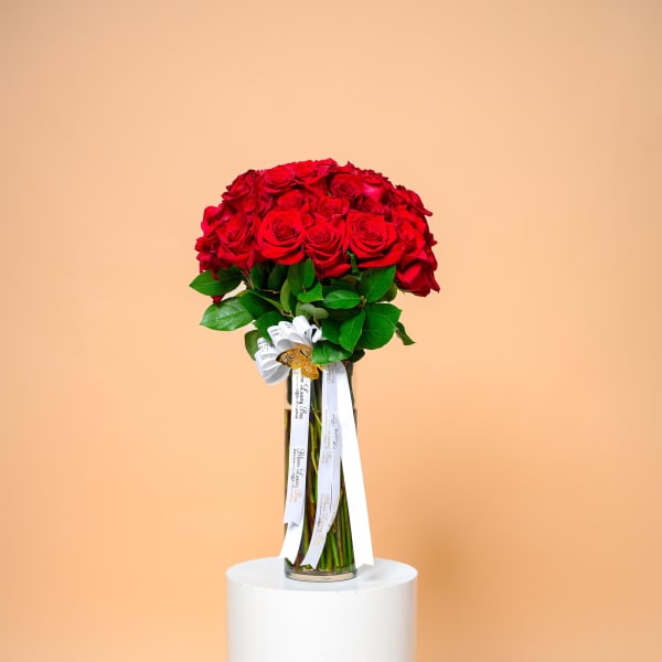 Tall bouquet of red roses in a glass vase with white ribbons
