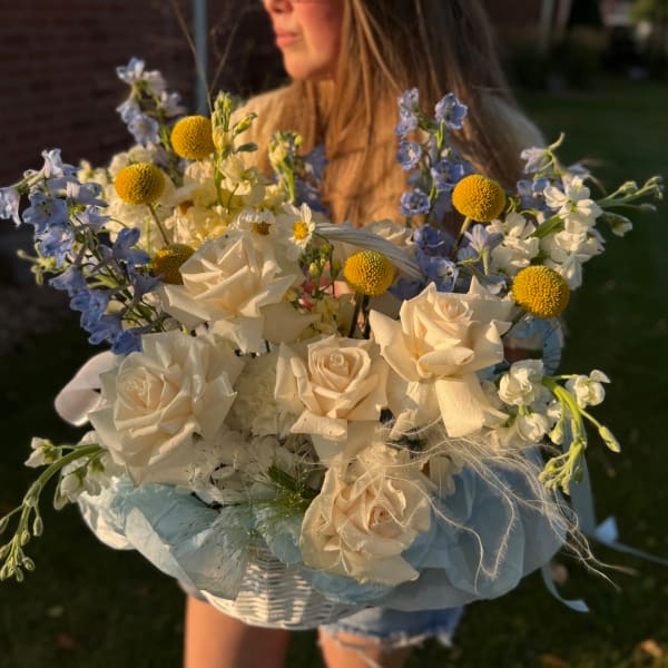 Bouquet of cream roses, blue flowers, and yellow pom blooms in a basket