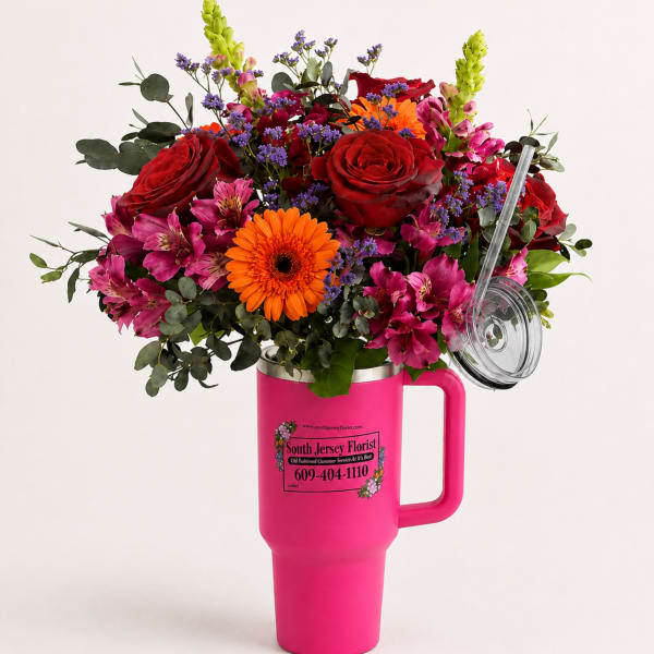 Mixed bouquet of red roses, orange gerbera daisies, and pink flowers in a pink tumbler vase