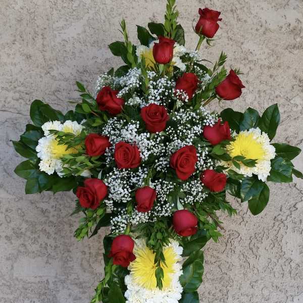 Cross-shaped floral tribute with red roses, white flowers, and yellow chrysanthemums