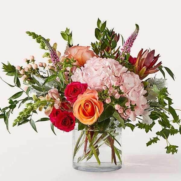 Mixed bouquet of pink, peach, and red flowers in a clear glass vase