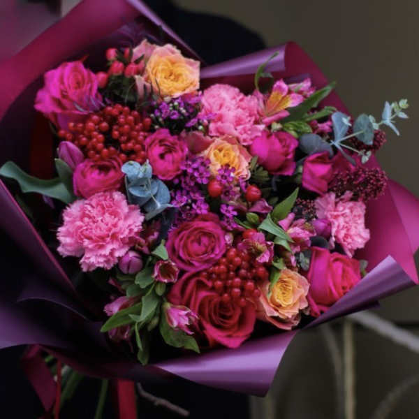 Bright bouquet of hot pink roses and carnations with yellow roses and berries wrapped in purple paper