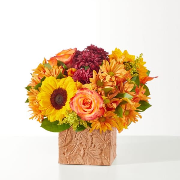 Mixed bouquet with sunflowers, roses, and mums in a textured square vase