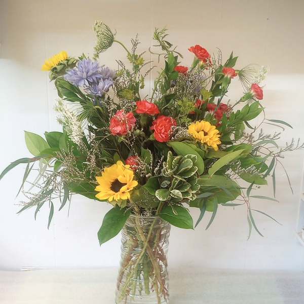 Mixed bouquet of sunflowers, red carnations, and purple blooms in a glass vase