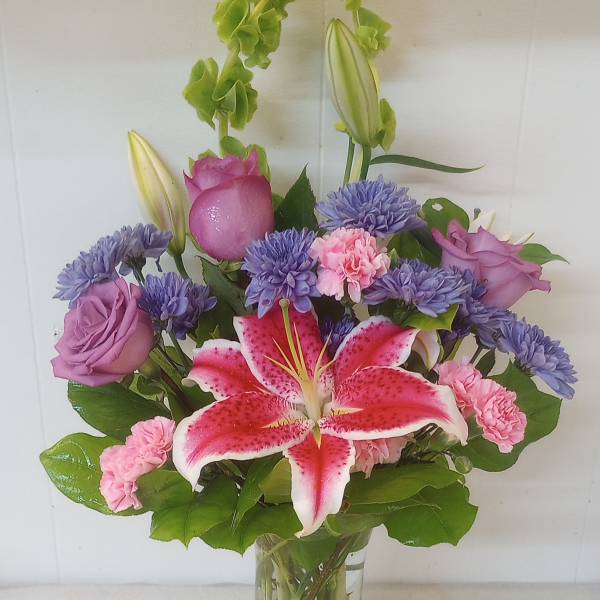 Mixed bouquet of pink lilies, roses, and purple flowers in a clear glass vase