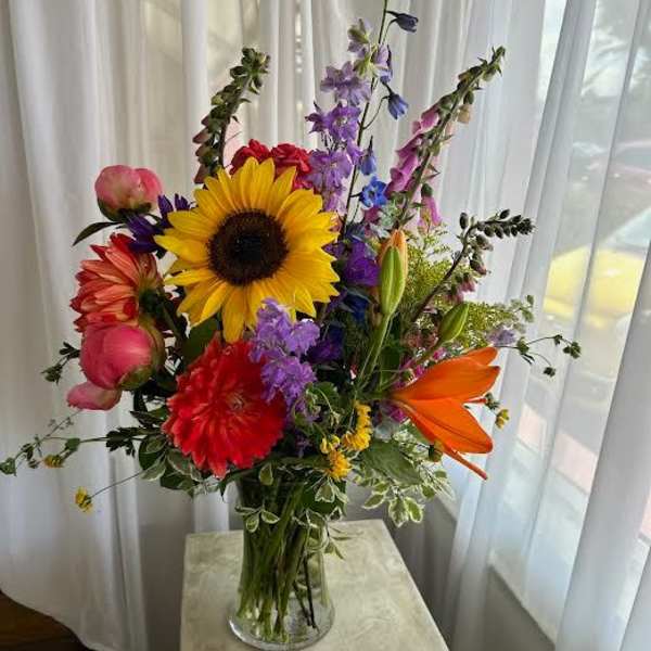 Colorful mixed bouquet in a clear glass vase with a sunflower and lilies