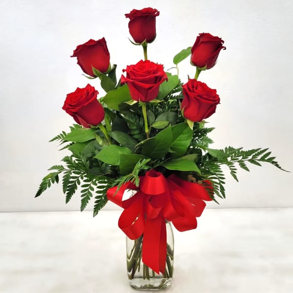 Red roses arranged in a clear glass vase with a red ribbon