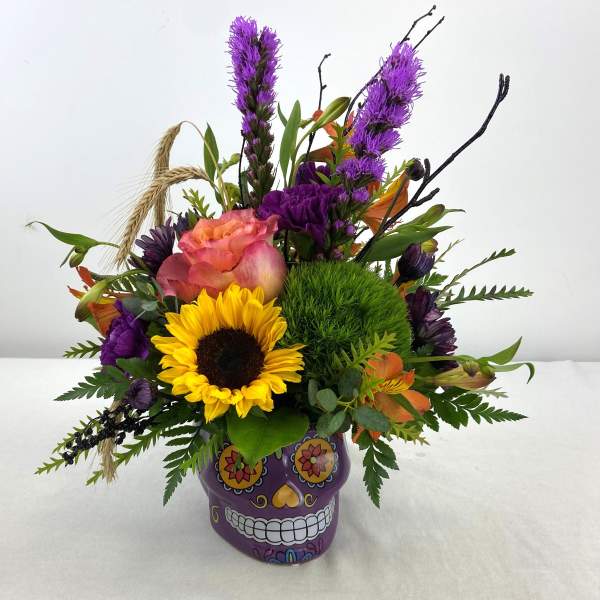 Colorful bouquet in a purple skull vase with a sunflower and purple blooms