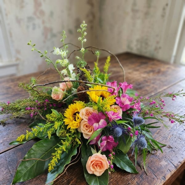 Low floral basket arrangement with yellow sunflowers, peach roses, and pink blooms
