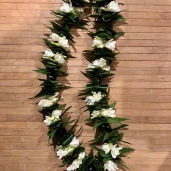 White floral lei with dark green leaves on a wooden floor