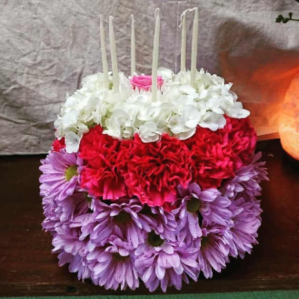 Round floral cake with white, pink, and purple flowers and tall candles