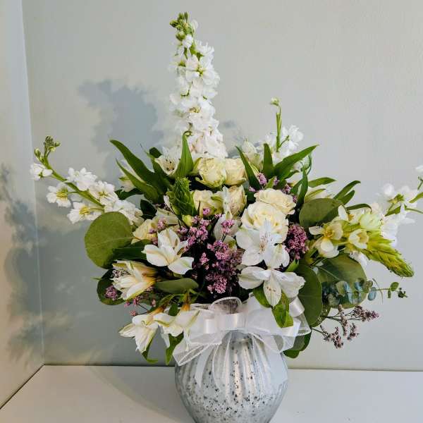 White floral arrangement in a speckled vase with a white ribbon