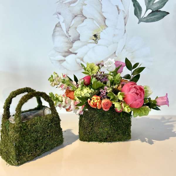 Flower arrangement in a moss-covered handbag-shaped container with pink and white blooms