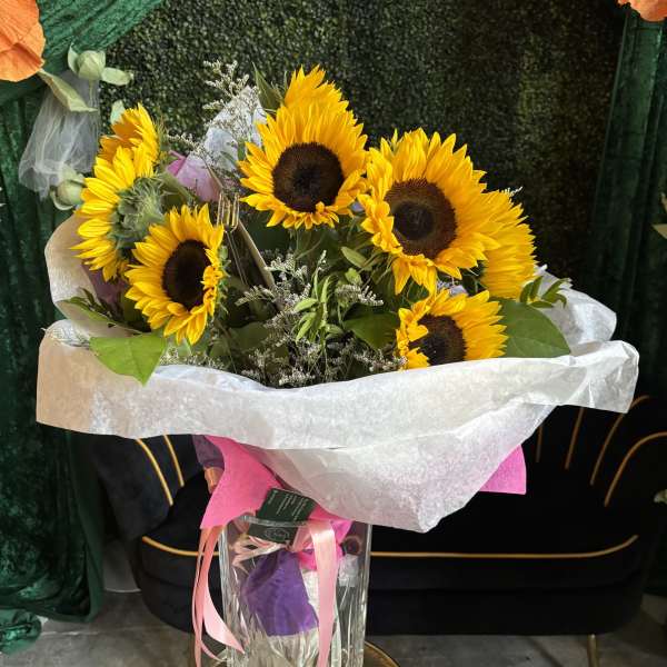 Bouquet of sunflowers in a clear glass vase with pink ribbon