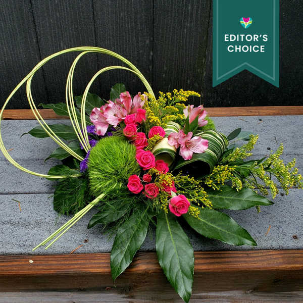 Low modern arrangement of hot pink roses and lilies with yellow accents and looping decorative grass.