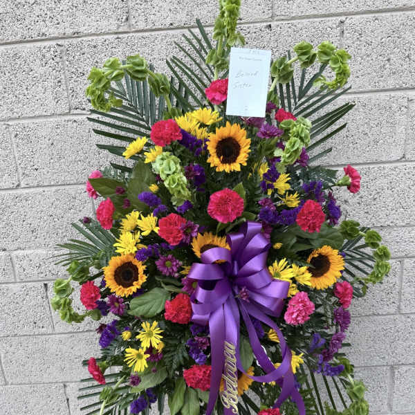 Standing sympathy spray with sunflowers, carnations, and purple ribbon