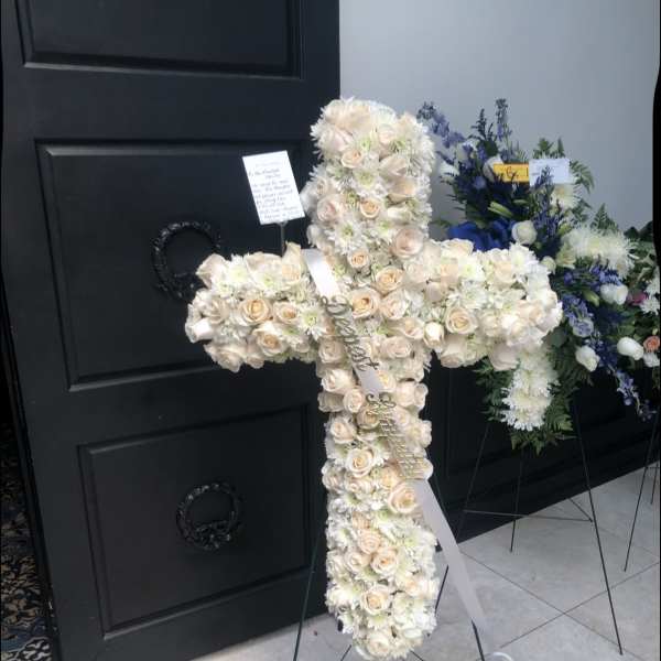 Cross-shaped floral tribute with cream roses and white flowers on a stand