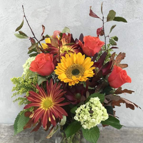 Mixed bouquet of roses, sunflowers, and chrysanthemums in a glass vase