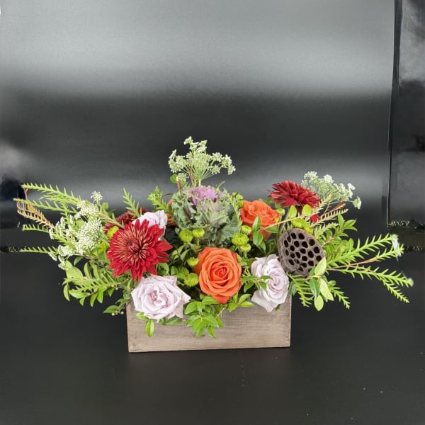 Mixed flower arrangement in a wooden box with orange and lavender roses