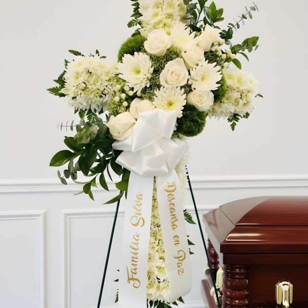 White funeral spray on an easel beside a casket