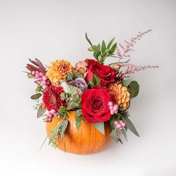 Floral arrangement in a pumpkin container with red roses and orange blooms