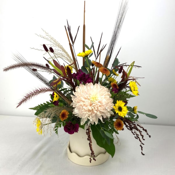 Mixed chrysanthemum arrangement in a cream vase with tall dried grasses
