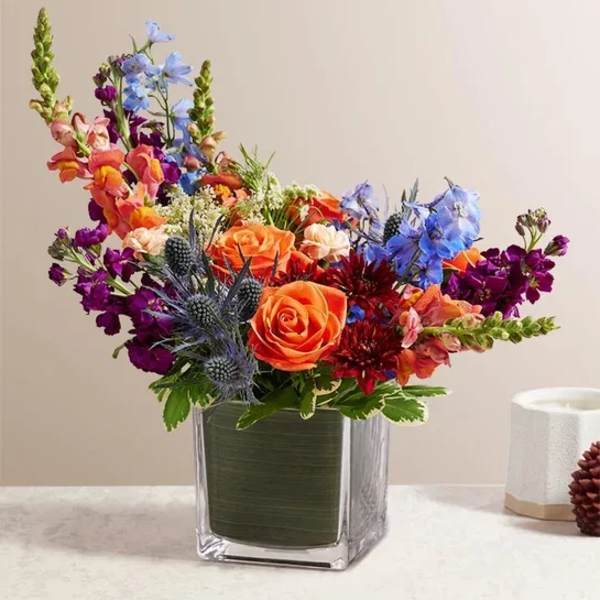 Colorful bouquet of roses and mixed flowers in a square glass vase