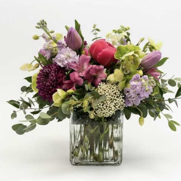 Mixed bouquet of pink, purple, and green flowers in a square glass vase
