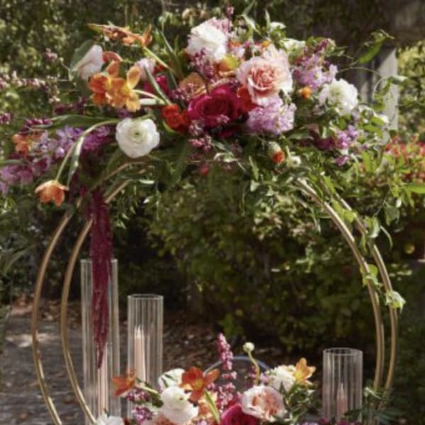 Two floral centerpieces on gold hoops with candles on a table