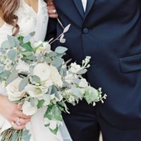 Bride holding a white and pale green bouquet beside a groom in a navy suit