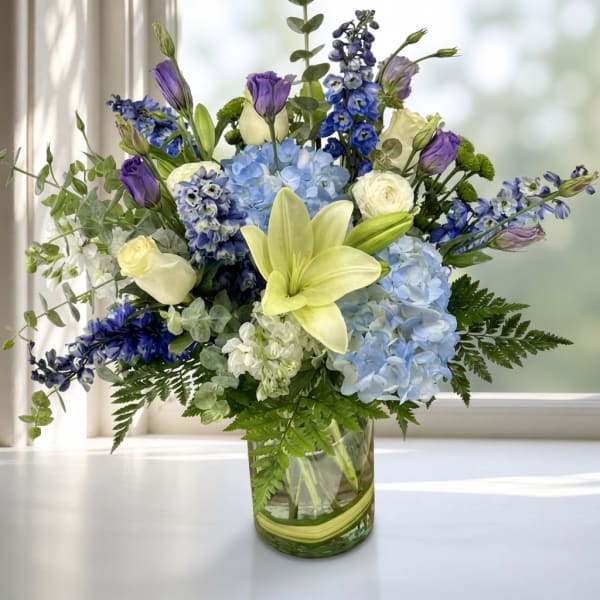 Blue and purple mixed bouquet with lilies and roses in a glass vase