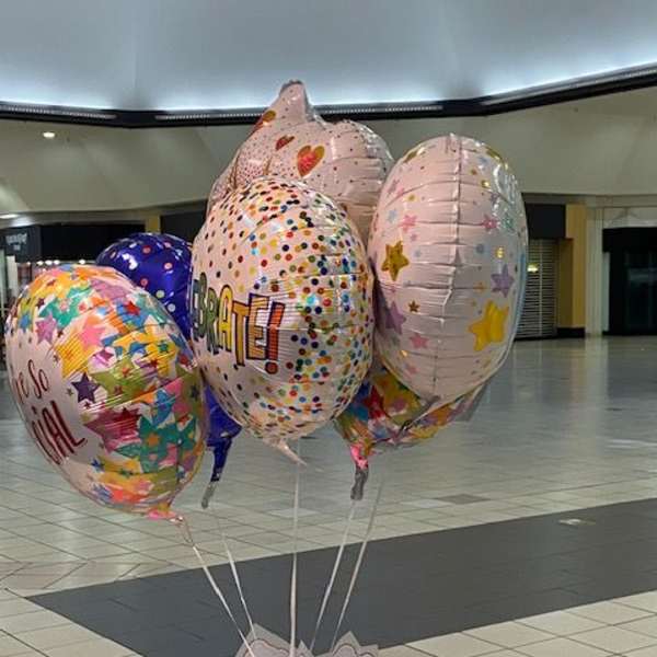 Cluster of birthday balloons with colorful patterns and a gift bag base