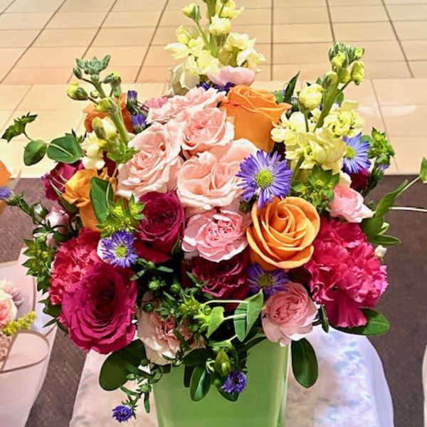 Mixed bouquet of roses, carnations, and purple daisies in a green vase
