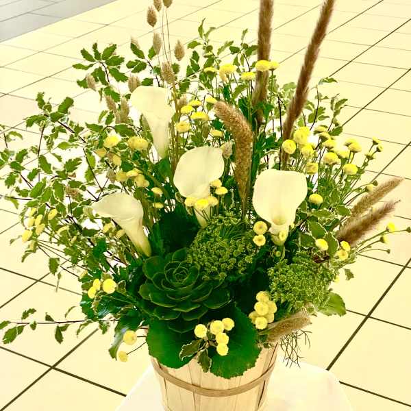Tall floral arrangement with white calla lilies and yellow blooms in a wooden basket