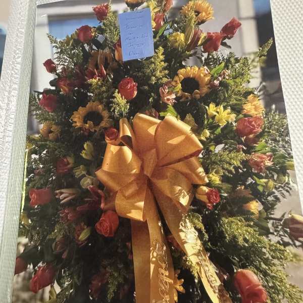 Large floral standing spray with sunflowers, roses, and an orange bow