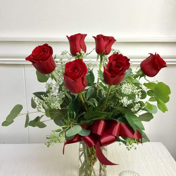 Red roses arranged in a clear glass vase with a red ribbon