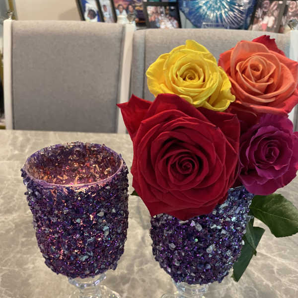 Two glitter-covered goblets hold colorful roses on a table.