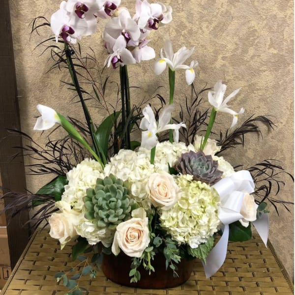Tall floral arrangement with orchids, hydrangeas, roses, and succulents in a low container