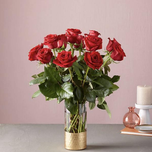 Red roses in a clear glass vase with a gold base