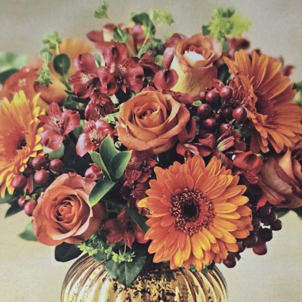 Orange roses and gerbera daisies in a gold vase