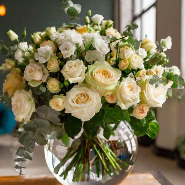 Cream roses and white blooms in a round glass vase