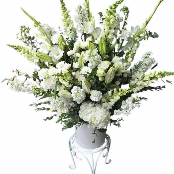 White floral arrangement in a white vase on a metal stand